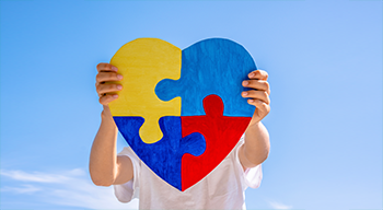 Dłonie chłopca trzymające kolorowe puzzle w kształcie serca na tle błękitnego nieba. Światowy Dzień Świadomości Autyzmu, koncepcja zaburzeń ze spektrum autyzmu.